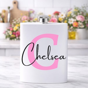 May include: A white stainless steel hip flask with a silver cap. The flask has a large pink letter "C" and the name "Chelsea" in black script. A personalized gift, ideal for carrying spirits.