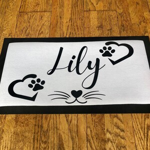 May include: Black and white doormat with the name "Lily" and paw prints in hearts. The doormat also has a black cat face with whiskers.