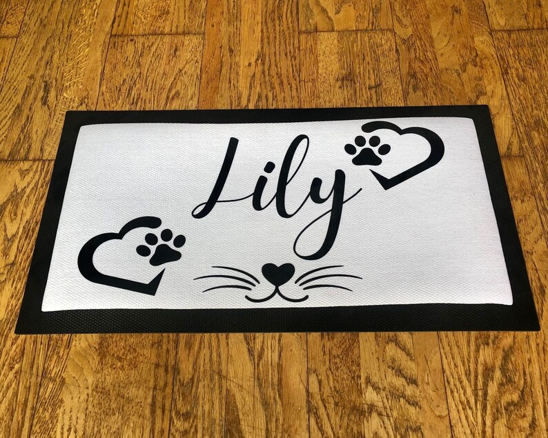 May include: Black and white doormat with the name "Lily" and paw prints in hearts. The doormat also has a black cat face with whiskers.