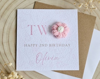 May include: A pink and white birthday card with the word "TWO" in pink lettering and a pink crocheted flower. The card says "Happy 2nd Birthday Olivia".
