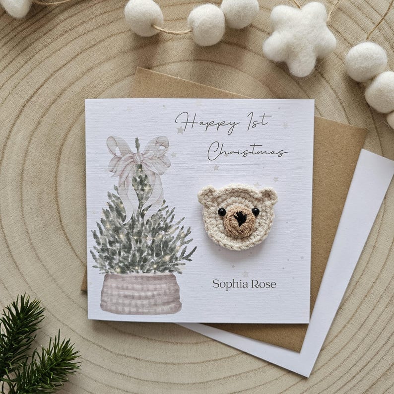 May include: A festive greeting card with the text "Happy 1st Christmas" and the name "Sophia Rose". The card features a watercolor illustration of a Christmas tree and a crocheted teddy bear face.