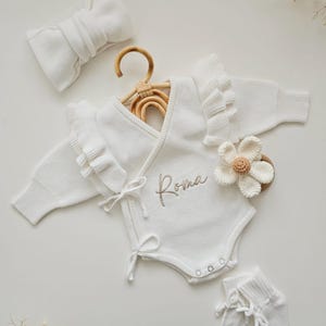 Personalised baby ruffle romper in white, part of a luxury neutral set for newborns. Features a baby announcement bodysuit, perfect as a baby coming home outfit with a knitted 'Hello World' ' She's Here ' design, ideal for baby showers or newborn photos