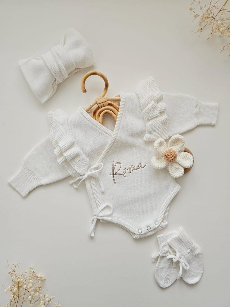 Personalised baby ruffle romper in white, part of a luxury neutral set for newborns. Features a baby announcement bodysuit, perfect as a baby coming home outfit with a knitted 'Hello World' ' She's Here ' design, ideal for baby showers or newborn photos