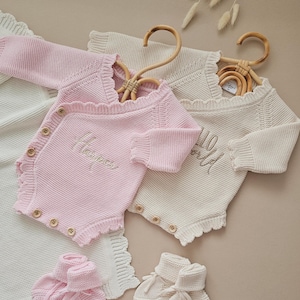 Personalised Baby Ruffle Romper in white, made from 100% cotton. Luxury neutral design with optional matching headband and booties. Custom embroidery options: 'Hello World,' 'She’s Here,' 'Isn’t She Lovely,' or baby’s name. Perfect for newborn coming home outfits, birth announcements, and baby shower gifts. Available in newborn size (fits up to 2-3 months). Matching rattle sold separately. Hand wash only. Ideal for baby girl outfits. Customizable baby romper set.