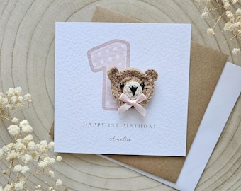 May include: A pink and white polka dot number one with a crocheted brown bear head and a pink bow on top. The card says "Happy 1st Birthday Amelia".