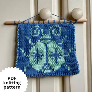 May include: Blue and light green knitted wall hanging with a bug design. The knitted piece is attached to a wooden dowel and hung with blue string. The text "PDF knitting pattern" is in the lower left corner.