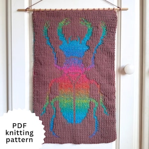 May include: A rectangular brown knitted wall hanging featuring a large, colorful beetle design in a gradient of blue, purple, pink, orange, yellow, and green. The piece is suspended from a wooden dowel. Text reads: PDF knitting pattern.