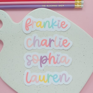 May include: Four die-cut vinyl stickers featuring the names Frankie, Charlie, Sophia, and Lauren in a colorful, rounded script font. Each name includes a small heart icon. Three pencils with the text THE BLOOMING BIKE are positioned above.