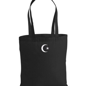 Puede incluir: Bolsa de tela negra con un diseño de media luna y estrella blancos.