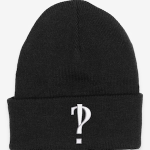 Puede incluir: Gorro de punto negro con un signo de interrogación bordado en blanco.