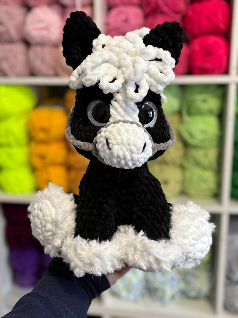 Another version of Hollie the Horse made with black and white yarn, featuring a curly mane and matching fluffy base. A creative variation showing how the digital crochet pattern can be customized.