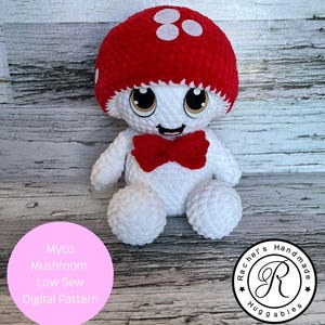 Puede incluir: Un peluche de hongo hecho a mano con una gorra roja y lunares blancos, un cuerpo blanco y una pajarita roja. El peluche tiene ojos grandes y expresivos y una cara sonriente. La imagen también incluye texto que dice "Artículo digital, no físico".