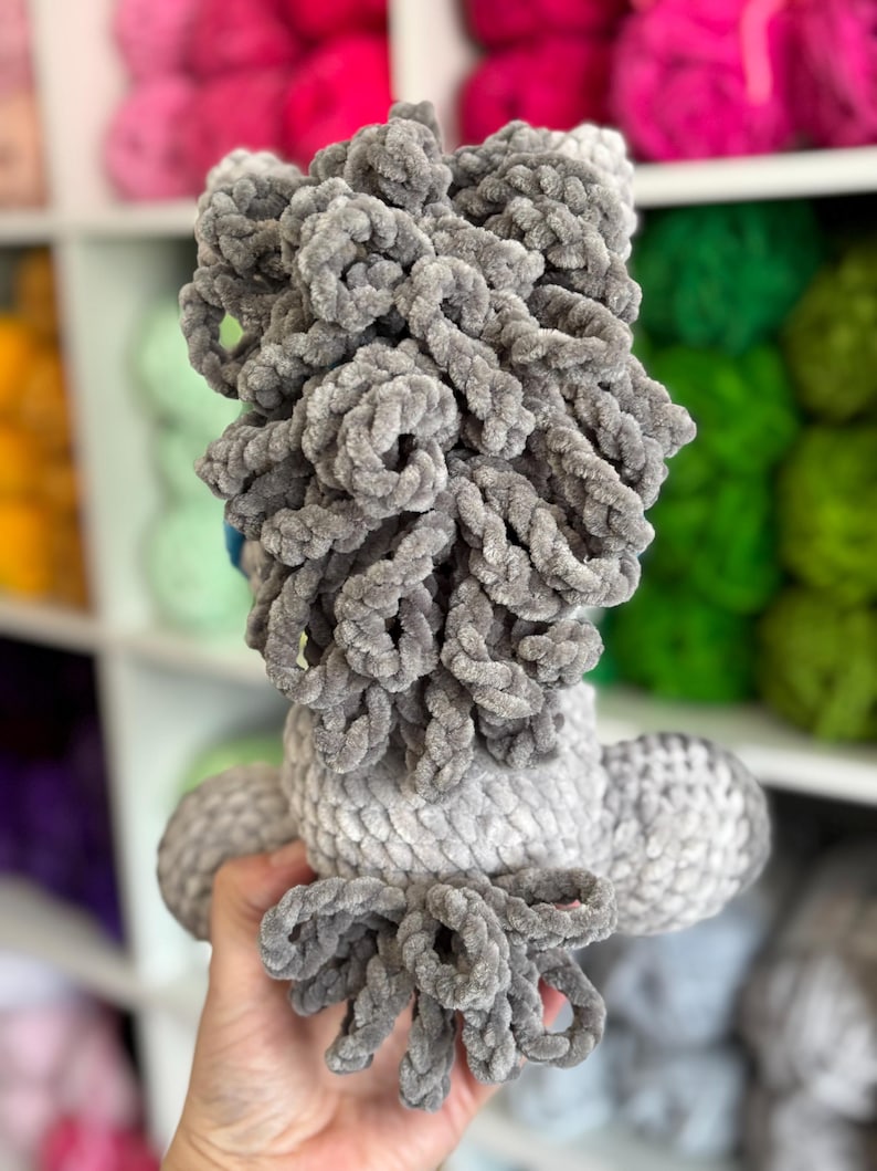 Rear view of the gray Hollie the Horse plushie, focusing on the curly yarn mane and tail. Demonstrates the plushie’s full 3D structure as created from the pattern.