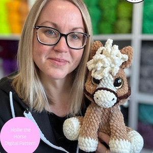 May include: A woman holds a handmade, crocheted horse plushie. The horse is brown with a white mane and muzzle, and has large, expressive eyes. The image includes text that reads "Hollie the Horse Digital Pattern" and "Digital item not physical item."