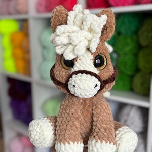 Front-facing photo of the finished Hollie the Horse plushie being held, made with soft brown and cream yarn. Showcases detailed mane and expressive eyes, highlighting the quality of the crochet pattern.