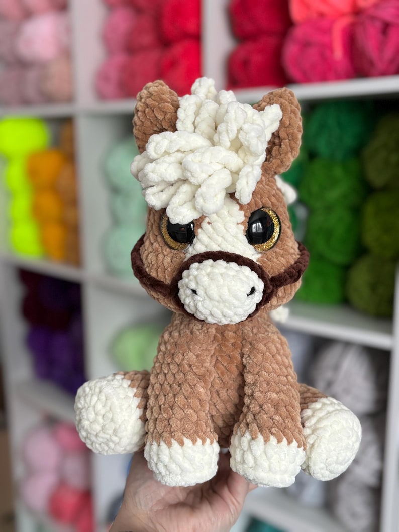 Front-facing photo of the finished Hollie the Horse plushie being held, made with soft brown and cream yarn. Showcases detailed mane and expressive eyes, highlighting the quality of the crochet pattern.