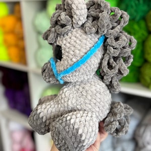 Side view of a gray Hollie the Horse plushie with a curly mane and tail, wearing a blue halter. Displays the finished plushie’s soft texture and charming shape.
