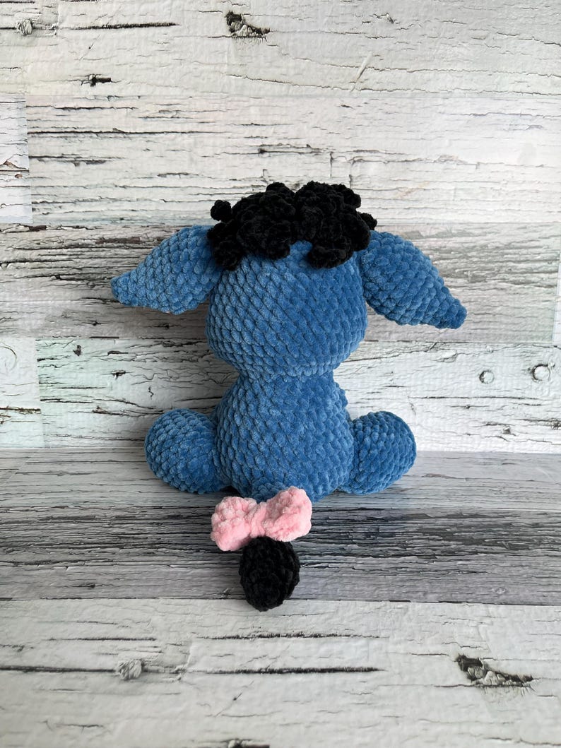 Rear view of blue Dylan the Donkey crochet plush with fluffy mane and pink bow on tail.