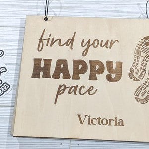 May include: Wooden sign with the text "find your happy pace" and the name "Victoria" below. The sign has two footprints in the bottom right corner.