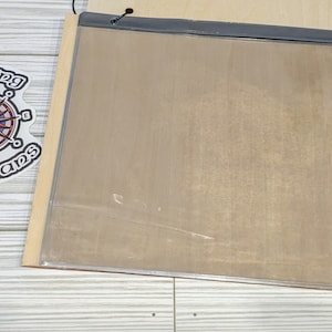 Pu&ograve; includere: Una lavagna rettangolare, vuota, di colore marrone chiaro, incorniciata con un coperchio in plastica trasparente. La lavagna &egrave; montata su una superficie in legno chiaro.