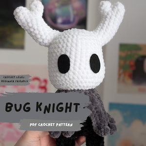 Könnte beinhalten: Handgefertigte Bug Knight-Häkelpuppe mit weißem Kopf, schwarzen Augen und einem grauen Umhang. Die Puppe hat ein anfängerfreundliches Häkelniveau und ist ein PDF-Häkelmuster.