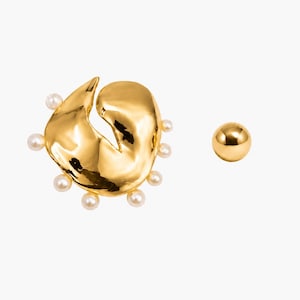 Könnte beinhalten: Ein Paar goldfarbene Ohrringe. Ein Ohrring hat eine freie Form mit kleinen, runden, weißen Perlen an den Rändern. Der andere Ohrring ist eine kleine, runde, goldfarbene Kugel. Die Ohrringe werden auf weißem Hintergrund präsentiert.