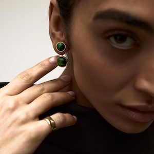 Puede incluir: Un par de pendientes de oro con detalles de piedras preciosas verdes. Los pendientes tienen una piedra preciosa redonda, ligeramente más grande, en la parte inferior y una piedra preciosa redonda más pequeña en la parte superior.