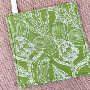May include: A square, green potholder with a white botanical design featuring artichokes, radishes, and other vegetables. The potholder has a white loop for hanging and is made of a durable fabric.
