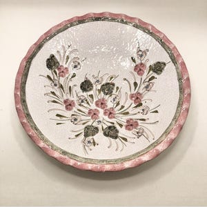 May include: A white ceramic plate with a pink and green floral design. The plate has a scalloped edge.