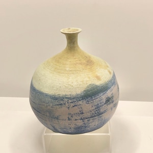May include: A handcrafted ceramic vase with a rounded body and a narrow neck. The vase features a color palette of beige, blue, and white, with a textured, layered appearance. The design suggests a rustic, artisanal aesthetic, suitable for home decor.