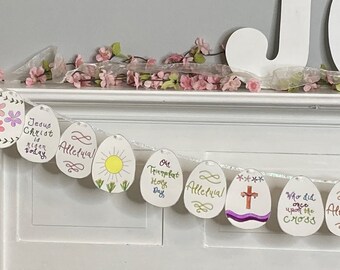 May include: A white paper Easter egg banner with a string of white paper eggs decorated with colorful drawings and text. The eggs have phrases like "Jesus Christ is risen today", "Alleluia", "Oh Trumpet Holy Day", "Who did once upon the cross", and "Alleluia".