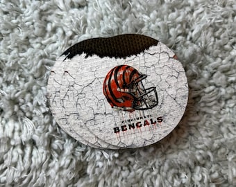 Könnte beinhalten: Ein runder, weißer Untersetzer mit einem abgenutzten, rissigen Lackdesign. Der Untersetzer zeigt einen schwarzen und orangenen Footballhelm mit dem Schriftzug "Cincinnati Bengals" darunter.