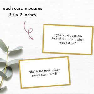 May include: Two conversation starter cards with gold borders on a white background. The text on the top card reads "If you could open any kind of restaurant, what would it be?" The text on the bottom card reads "What is the best dessert you've ever tasted?" Each card measures 3.5 x 2 inches.
