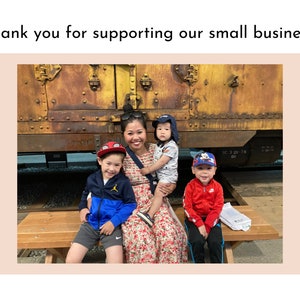 May include: A woman and three children pose in front of a rusty train car. The woman is wearing a floral dress and the children are wearing casual clothing. The children are smiling and the woman is looking at the camera.