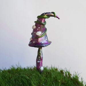 May include: A whimsical purple and green mushroom with white dots, standing on a bed of green moss. The mushroom has a unique, curled cap and a textured stem.