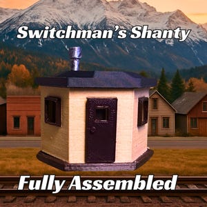 May include: A fully assembled, beige, miniature wooden shanty with a black door and a black roof. The shanty has two windows on the front and the text "Switchman's Shanty" is written above the shanty. The text "Fully Assembled" is written below the shanty.