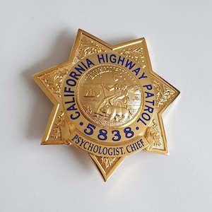 Peut inclure: Un insigne en forme d'étoile à sept branches de couleur dorée, arborant le sceau de la California Highway Patrol au centre. Le texte bleu indique CALIFORNIA HIGHWAY PATROL, le numéro 5838 et le titre PSYCHOLOGIST CHIEF. Orné de gravures de feuilles.