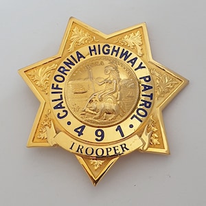Op de afbeelding: Een goudkleurige badge in de vorm van een zespuntige ster met het zegel van de staat Californië in het midden. De tekst CALIFORNIA HIGHWAY PATROL staat in blauw langs de cirkelvormige rand, met het nummer 491 en het woord TROOPER op een banner.