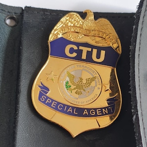Könnte beinhalten: Ein goldfarbenes Metallabzeichen mit einem Adler an der Spitze, einem blauen Emaille-Banner mit dem Text CTU und einem zentralen Siegel mit dem Text COUNTER TERRORIST UNIT. Ein blaues Banner am unteren Rand zeigt den Text SPECIAL AGENT in Gold.