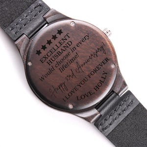 May include: A dark brown wooden watch with a black leather band. The watch face has a message engraved on it that reads "Excellent Husband Would choose in every lifetime! Happy 53rd Anniversary! I love you forever Love, Holly".