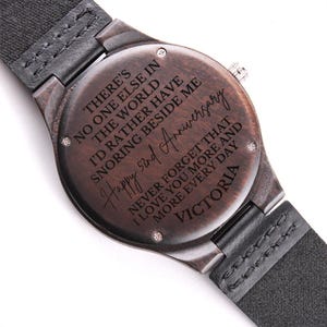 May include: A dark brown wooden watch with a black leather band. The watch face has a message engraved on it that reads "There's no one else in the world I'd rather have snoring beside me. Happy 52nd Anniversary. Never forget that I love you more and more every day. Victoria."