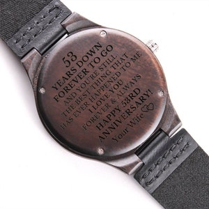 May include: A brown wooden wristwatch with a black leather band. The watch face has a message engraved on it that reads "53 Years Down Forever to Go And You're Still The Best Thing That Has Ever Happened To Me I Love You Forever & Always Happy 53rd Anniversary! Your Wife".