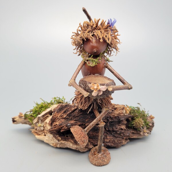 Oakie acorn elf sitting on a log, holding a basket. Great nature photo prop. "Say it with Oakies" fantasy art sculpture.