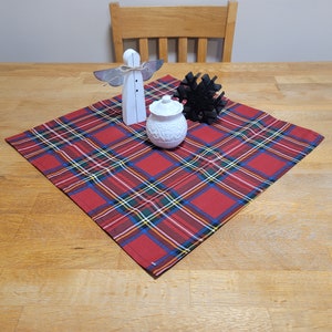 Pode incluir: Um corredor de mesa vermelho e preto xadrez com um pote de cerâmica branco, uma figura de anjo de madeira e um objeto decorativo preto no topo.