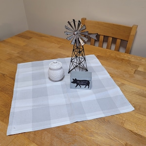 May include: A white and gray checkered table runner with a white ceramic jar, a black metal windmill, and a gray wooden block with the text "You had me at bacon" on a wooden table.