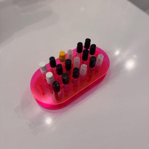 May include: A pink plastic tray with a variety of small perfume bottles with black, white, and yellow caps. The bottles are arranged in rows.