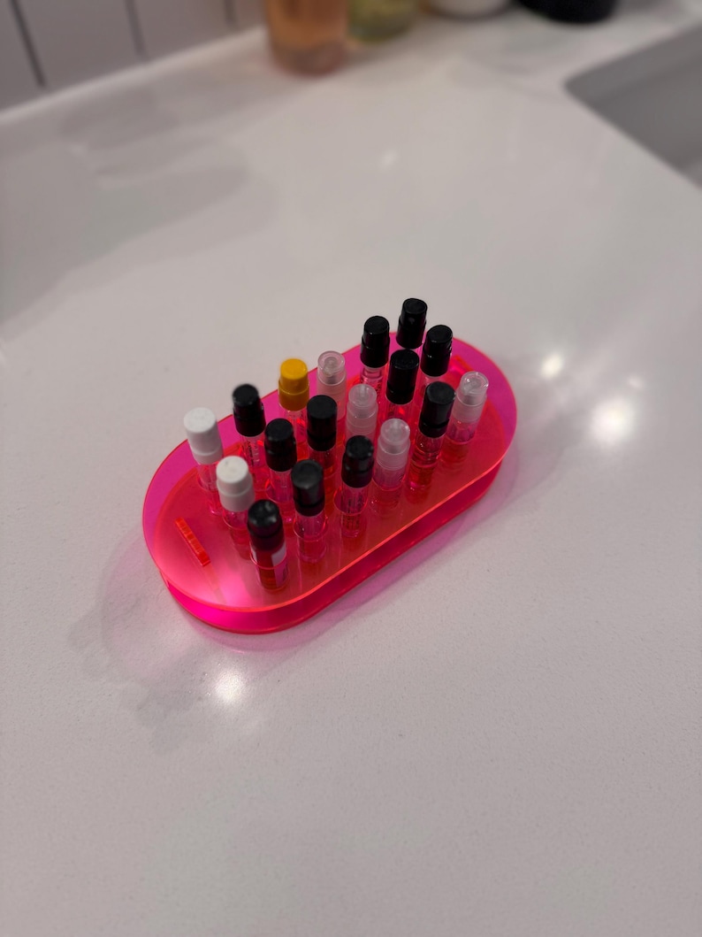 May include: A pink plastic tray with a variety of small perfume bottles with black, white, and yellow caps. The bottles are arranged in rows.