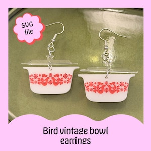 Op de afbeelding: Oorbellen in de vorm van kleine witte vintage kommen met rode vogel- en bloemmotieven. Ze hebben doorzichtige deksels en zilverkleurige oorhaken. De tekst "SVG file" staat in een roze wolk.