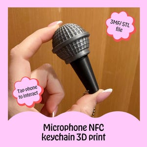 Pode incluir: Um porta-chaves de microfone cinza e preto com o texto "Microphone NFC keychain 3D print". O porta-chaves tem uma cabeça de microfone detalhada e uma alça preta. A imagem também inclui o texto "Tap phone to interact" e "3MF/ STL file".