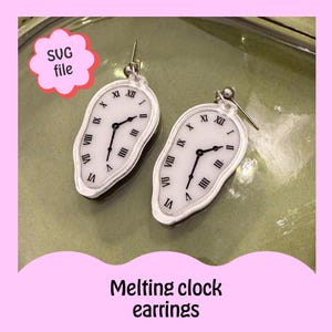 May include: Two white melting clock earrings with black hands and Roman numerals. The earrings are on a green surface, with the text "Melting clock earrings" at the bottom. A pink flower-shaped graphic with the text "SVG file" is in the upper left corner.